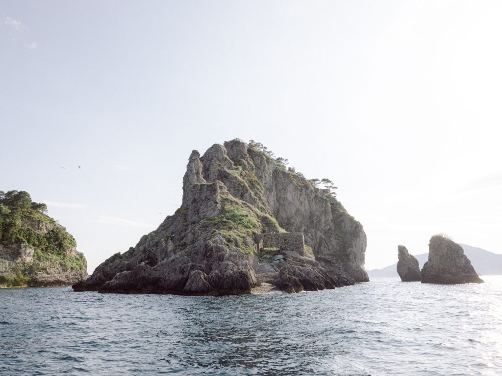 Islet off the Amalfi Coast in soft late-afternoon light in May, seen from a boat.