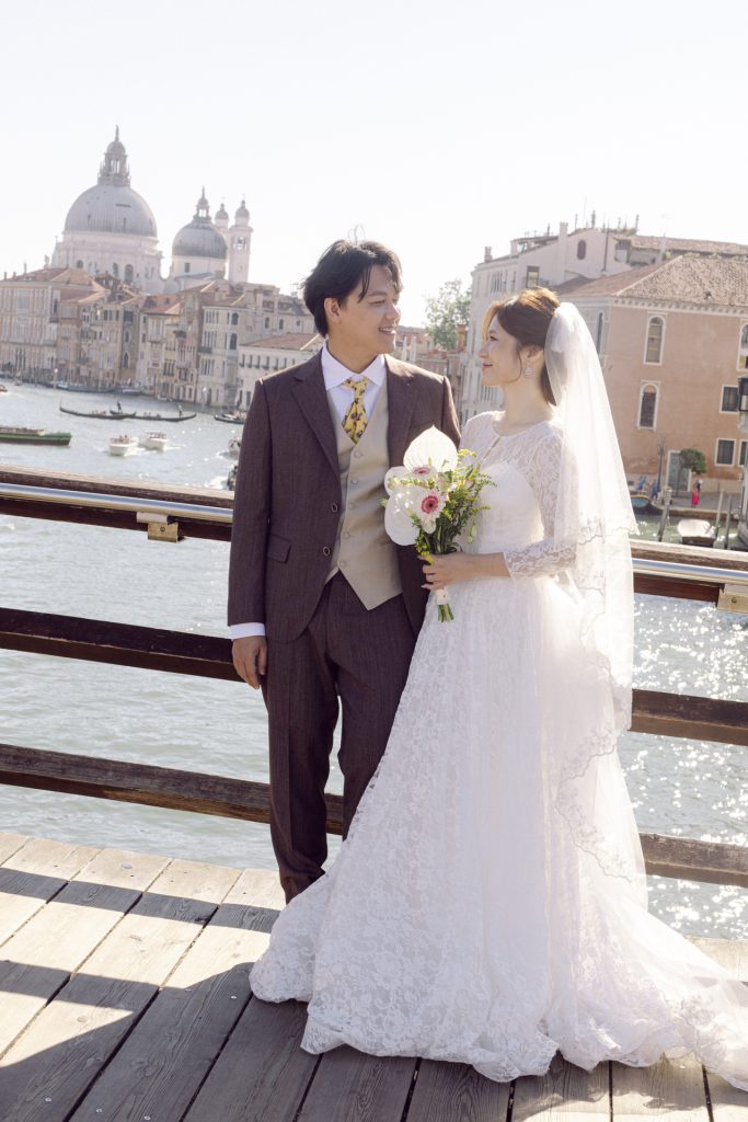 Couple in wedding attire on the Accademia Bridge in Venice with Santa Maria della Salute in the distance