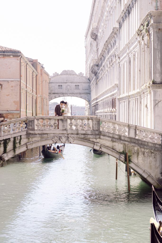 Wedding couple on a bridge Canonica bridge close to Piazza San Marco Venice, with Ponte dei Sospiri behind them