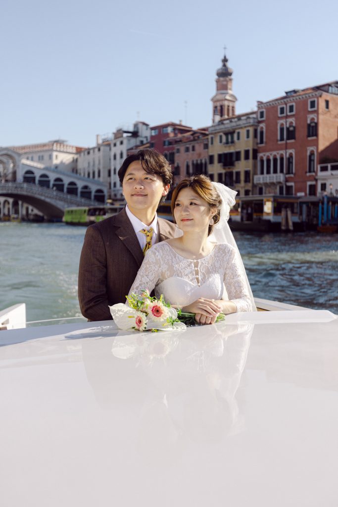 Couple in wedding attire on a water taxi on the Grand Canal in Venice Rialto in the back