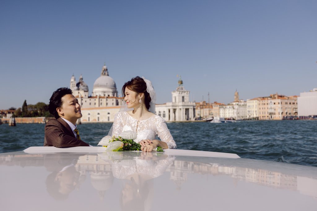Couple in wedding attire on a water taxi on the Grand Canal in Venice basilica della salute in the back