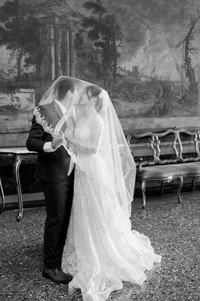 Bride and groom kissing among the frescoes of Ca' Sagredo hotel, Venice