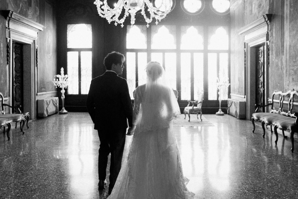 Bride and groom walking in front of the majestic windows of Ca' Sagredo hotel, Venice